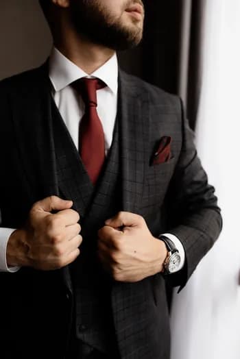 https://backend.antailors.ae/wp-content/uploads/2025/05/bearded-man-stylish-tuxedo-red-tie-strong-man-s-hands.webp